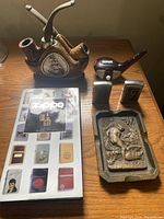 Photo showing full set including ceramic pipe stand holding 2 pipes, 3 Zippo lighters, brass ashtray, and Zippo booklet.