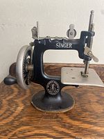 Front view of black cast-iron machine on pedestal base showing Singer logo and hand wheel