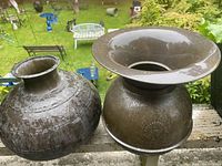 Wide shot showing both metal containers on an outdoor ledge with grass and outdoor furniture in the background.