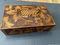 Closed view of a wooden box with grapevine carving on the lid
