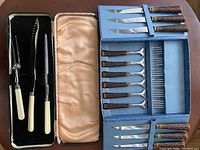 Full view of two separate cutlery sets: a three-piece carving set with ivory handles in a black velvet-lined box, and a 6-piece steak cutting utensil set with stag handles in a blue box.