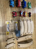 Photo showing wooden train engines, carriages, track pieces, and battery-powered crossing gate on wood floor.