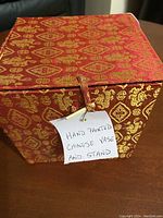 Closed red and gold decorative box with a tag stating 'Hand Painted Chinese Vase and Stand'.