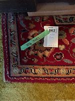 Close-up photo of corner of large area rug showing size tag 10'6" x 14'2", floral pattern with red background