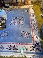Full view of the large rectangular blue area rug with floral designs and fringe on one edge