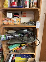 Photo of wooden shelves showing various automotive fluids, brushes, and tools arranged in boxes and loose.