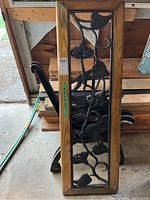 Close view of one decorative metal side panel with carved wooden edge trim showing black painted cast iron floral and vine design.