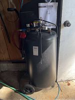 Front view of compressor showing black steel tank, control panel with gauges, attached red hose and wheels.