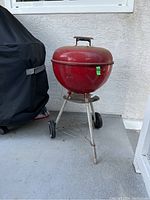 Full side view of red dome charcoal barbecue grill with lid and metal legs with wheels.