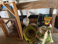 Wooden gardening screen with wire mesh visible alongside coiled green and white garden hoses and bags of gardening products on the floor
