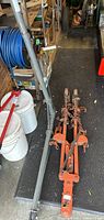Full view of hoist frame with orange clamps and attached chains on black mat in workshop setting.