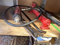 Photo of red hydraulic hand pump with attached hose and three metal pry bars on wooden surface.