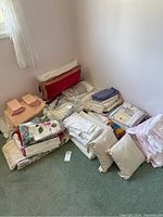 Wide view of various linens including tablecloths, serviettes, pillows, folded towels, sheets, and pillows stacked on the floor.