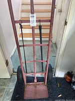 Front view of the red metal hand cart with two wheels and a flat toe plate, showing signs of wear and used condition.