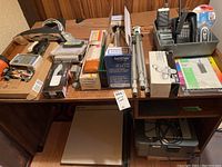 Full view of all items on wooden desk including electronic devices, tripod, toner cartridge, and office accessories.