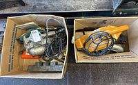 Three electric power tools in two cardboard boxes; one is a B&D belt sander, others are different models.