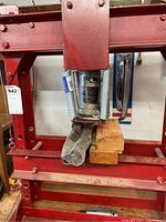 Front view showing the 6 ton hydraulic bottle jack labeled 'Power Line' with springs on both sides mounted on the red metal frame and wooden blocks resting on the press bed.