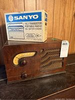 Photo showing vintage wooden radio with curved yellow dial and control knobs, and the Sanyo portable radio box behind it