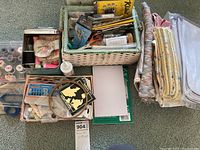 Photo showing sewing boxes containing various notions such as scissors, thread spools, pins, labels, and other sewing tools, accompanied by folded fabric pieces