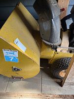 Side view photo showing yellow steel chute with Bolens 7 horsepower sticker and chute adjustment lever.