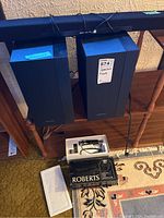 Photo showing two Samsung speakers (PS-WM20 and PS-WH450) and one Samsung sound bar (HW-M360) placed on a wooden shelf and floor; included packing materials and a Roberts branded box.