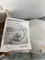 Owner's manual for Bissell deep cleaning machine model 1655C and part of the steam cleaner unit visible.