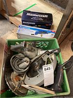 Green crate containing a used circular saw, blade, other parts, and boxed Mastercraft angle grinder and multi-crafter kit