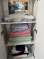 Photo of folded towels and twin sheet set on shelves in a cabinet.
