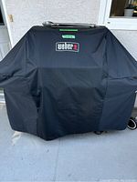 Black grill cover with Weber logo fully covering grill on patio