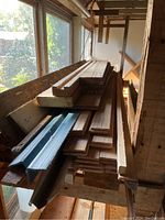 Wood lumber and planks stacked horizontally on a shelf indoors near a window.