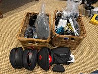 Overview of two wicker baskets containing headphones, cases, power supplies, and cables as packed for sale.
