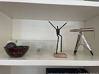 Wide shot showing all 4 items on white shelf - telescope, figurine, Berlin Wall souvenir, cocoa wood bowl with balls