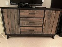 Front view of cabinet showing three drawers in center and two doors on each side with handles, standing on angled legs.