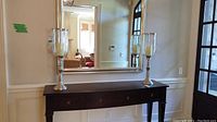 Pair of silver-tone metal hurricane candle holders on console table in front of mirror