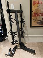Gray metal Saris bike rack with black adjustable straps and clamps, designed to hold multiple bikes, standing upright on tile floor.