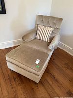 Photo of beige upholstered armchair with ottoman and striped accent pillow on hardwood floor.