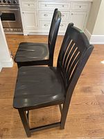 Two black wooden counter chairs side by side in kitchen area, showing side profile and seat shape.