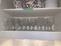 First photo of one shelf with 11 pressed glass goblets with intricate designs and clear glass