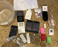 Overview of lot showing multiple Apple iPods, remotes, cables, earphones, cases and manuals arranged on a surface.