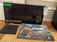 Razer BlackWidow keyboard box along with Ubisoft Far Cry 4 MSI mouse pad and Razer keyboard case placed on a floor.