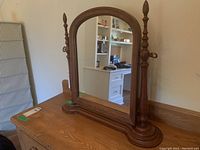 Front angle view showing the arched wood frame, turned finials, and base of the mirror with reflective surface.