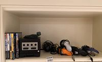 Shelf overview showing console, controllers, cables, memory card and five game cases