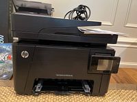Front view of HP Color LaserJet Pro MFP M177fw printer showcasing the front paper tray, control panel, and scanning unit on top with cables coiled.