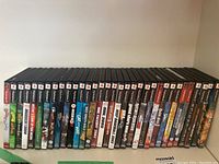 Front view of 26 PlayStation 2 game cases lined up on shelf showing titles and spine artwork.