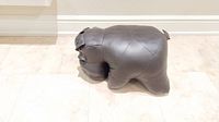 Side angle view of dark brown hippo-shaped foot stool on tiled floor.