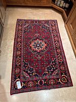 Full view of Persian rug laid flat on tile floor, showcasing entire pattern and border.