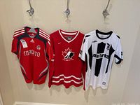 Three jerseys hanging on hooks against a wall, front view showing logos and designs.