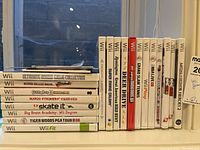 Close-up of 13 Wii game cases including titles like Ultimate Board Game Collection, Super Smash Bros. Brawl, Guitar Hero III Legends of Rock, Mario Strikers Charged, Skate It, Big Brain Academy, Tiger Woods PGA Tour 08, and Wii Fit