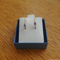 Pair of pear-shaped tanzanite earrings set in 14K yellow gold displayed in a blue box.