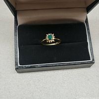Ring viewed from above in a black velvet display box showing emerald center and surrounding diamonds